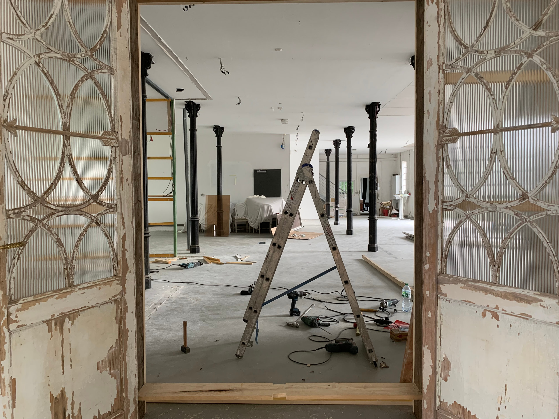 Blick durch alte gefasste Doppeltüren in die Halle mit historischen Gusseisensäulen während der Renovierung